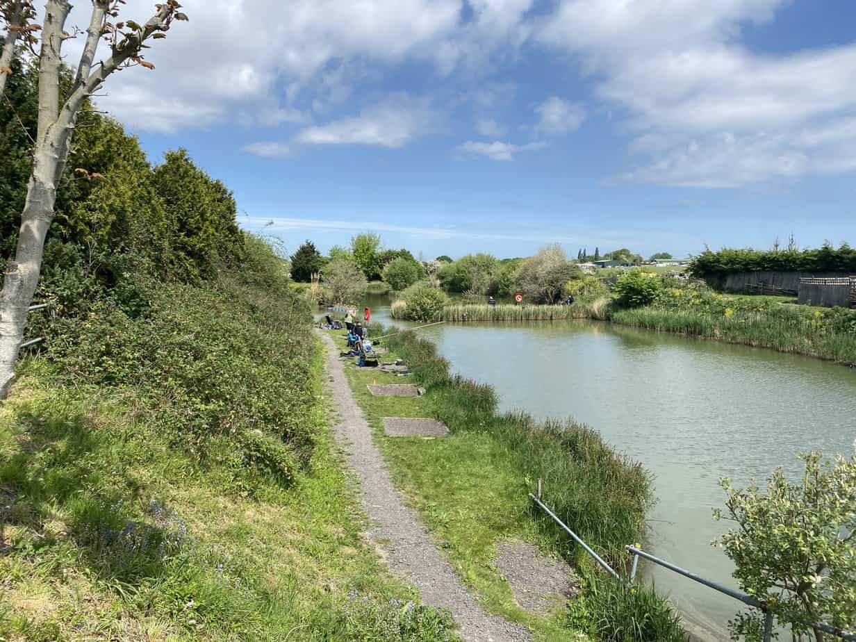 Anglers on the bank beside a lake at Finch Farm Fishery on a sunny day